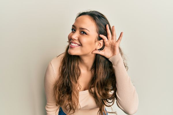 Young hispanic girl wearing casual clothes smiling with hand over ear listening and hearing to rumor or gossip. deafness concept.
